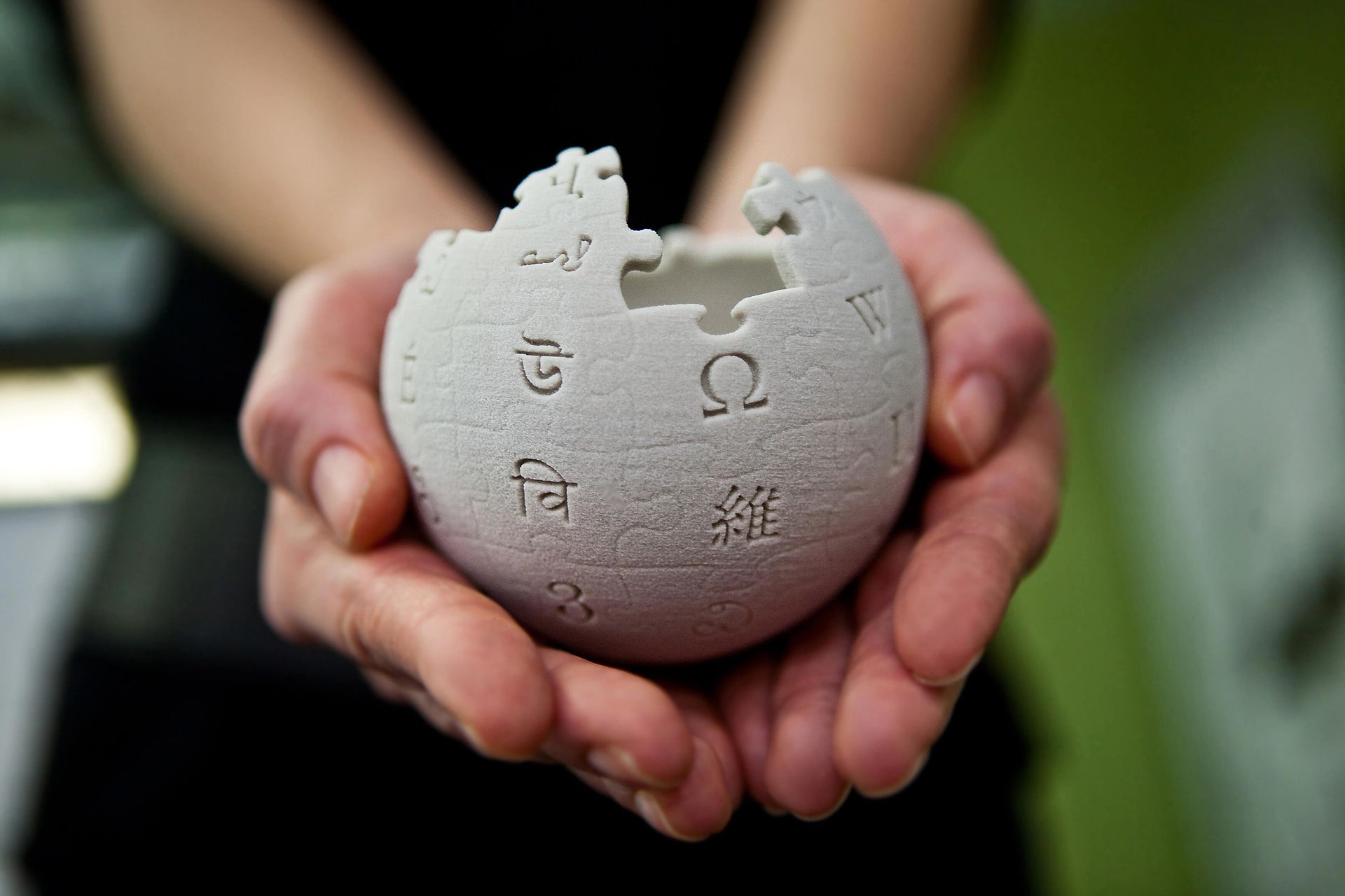 Un globe Wikipedia gris tenu entre des mains ouvertes